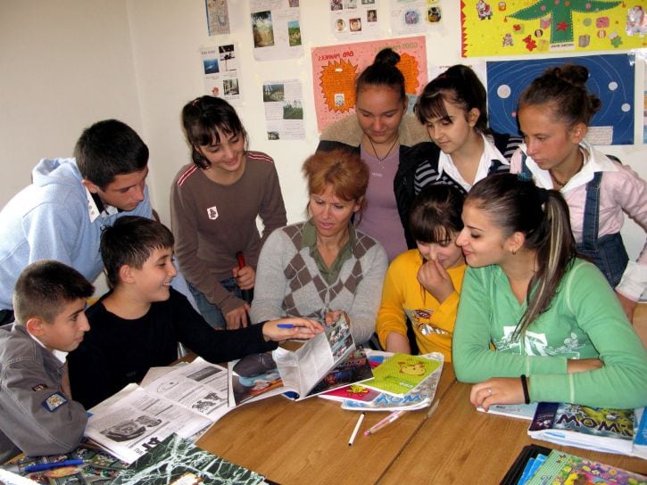 Female teacher sitting at table, surrounded by students